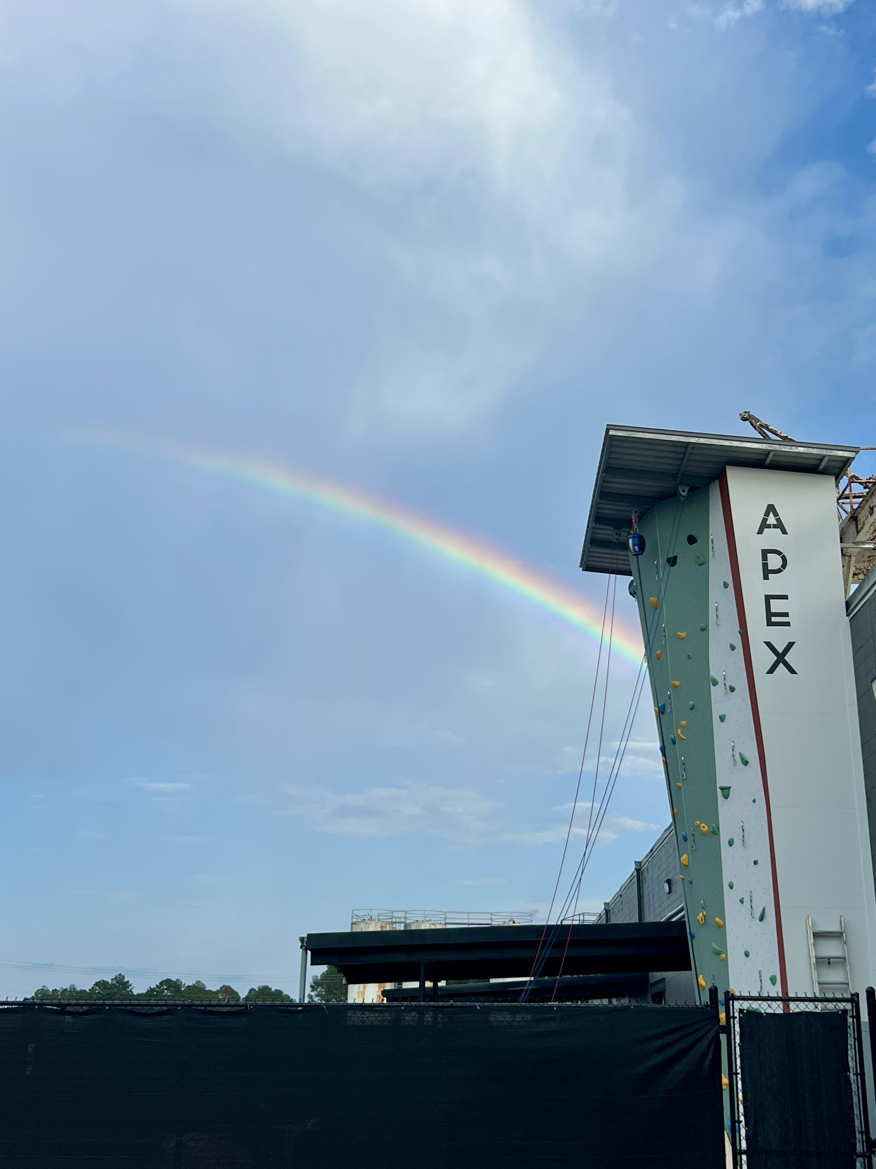 A vivid rainbow arcing across a blue sky over the APEX outdoor climbing tower