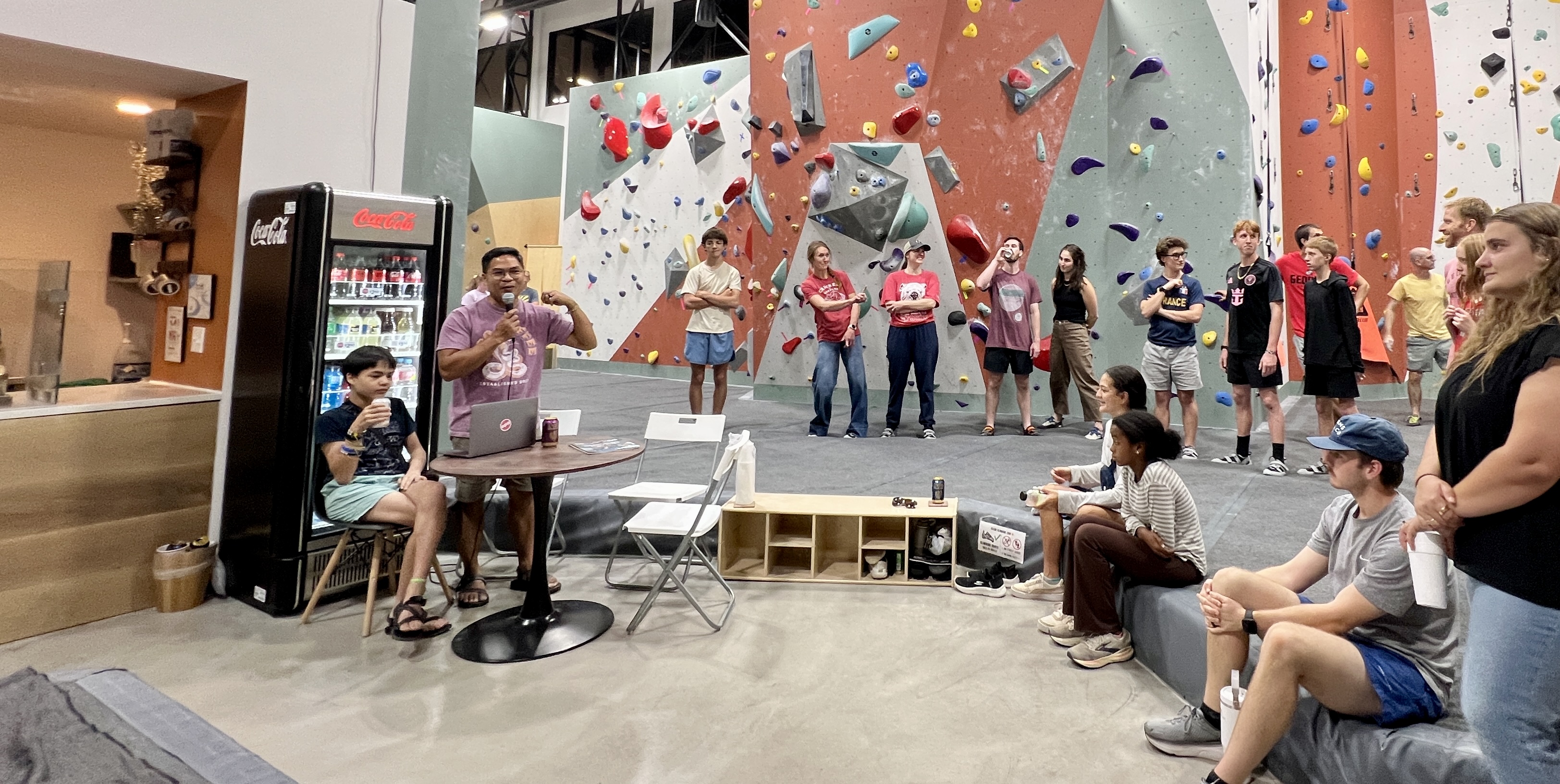 A speaker with a microphone addressing a seated circle of members inside the climbing gym at a past Field Notes gathering