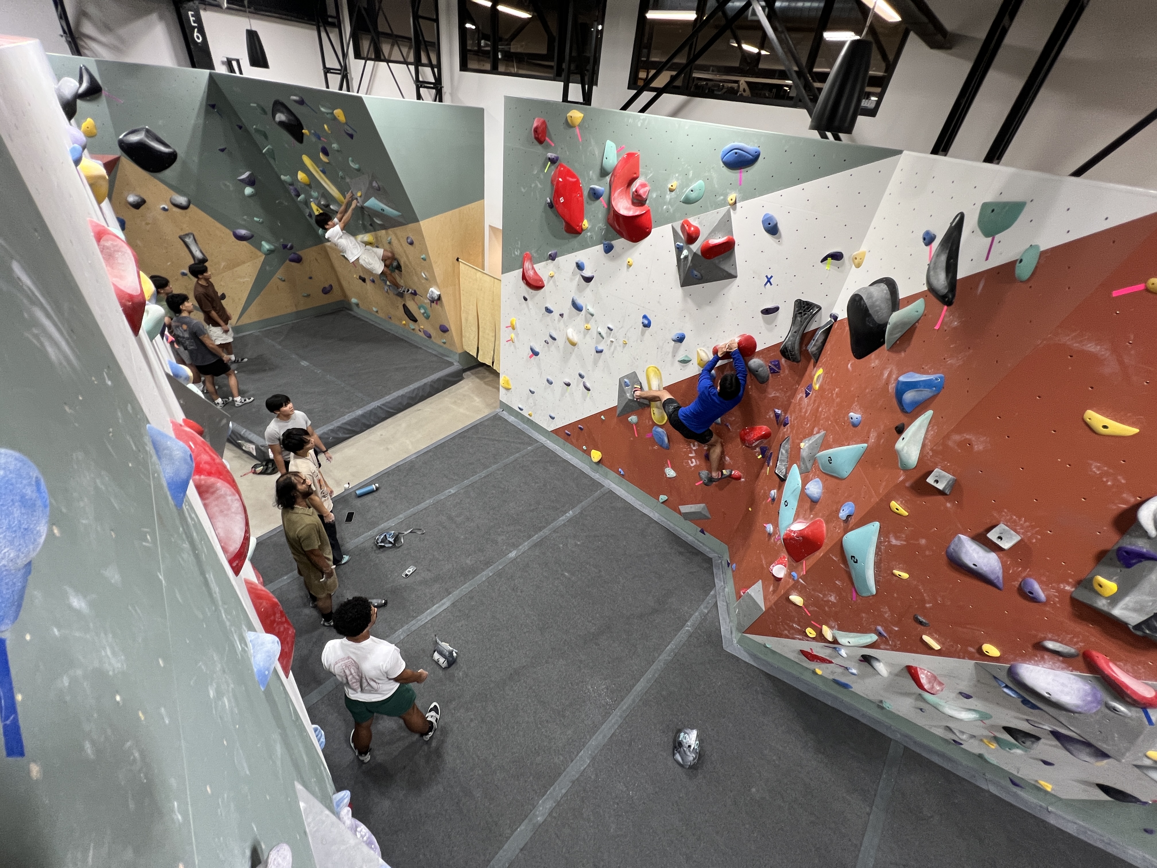 A climber working a route while other students watch from the padded floor