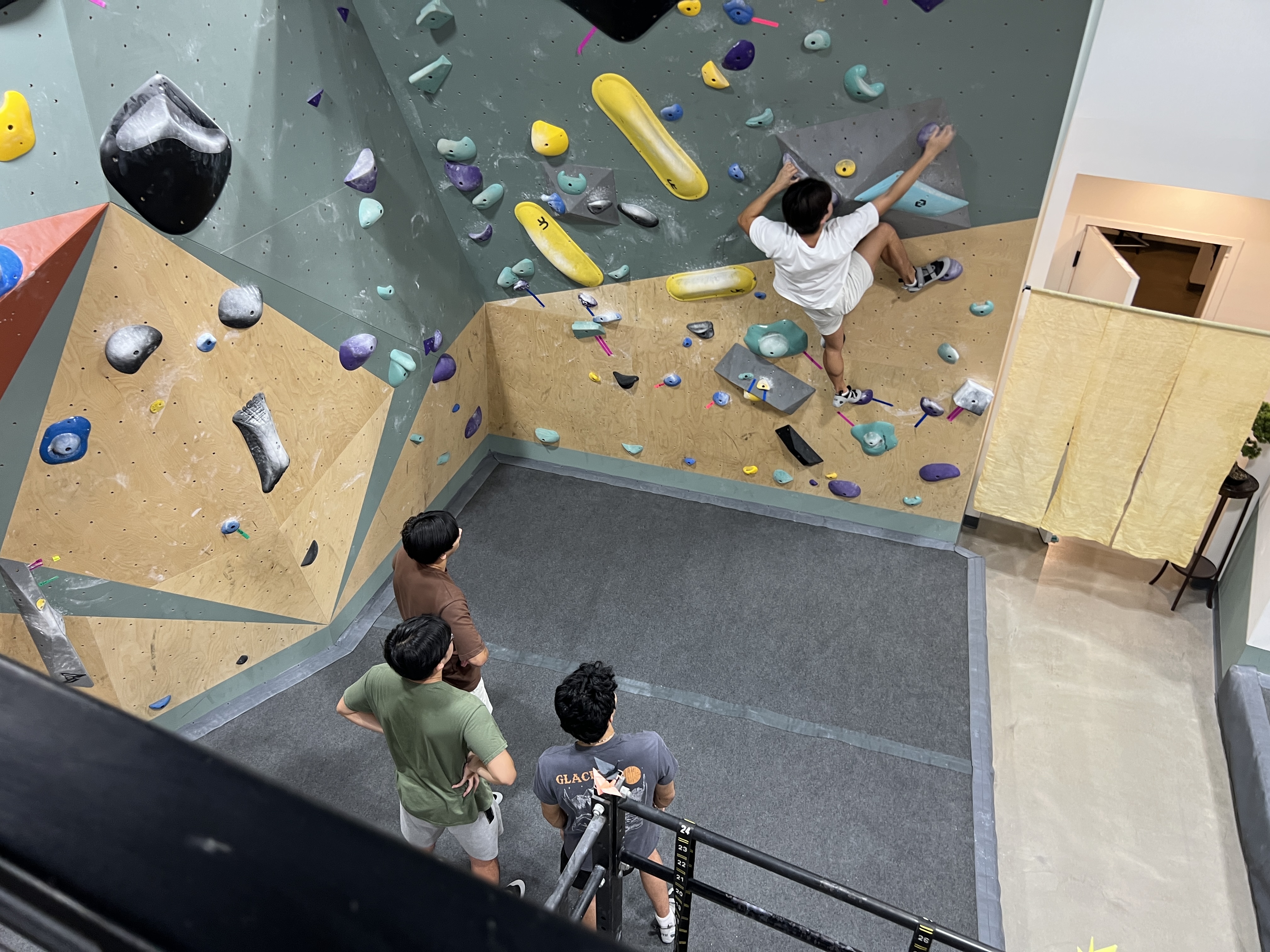 A climber reaching for holds on the wall while friends watch from below