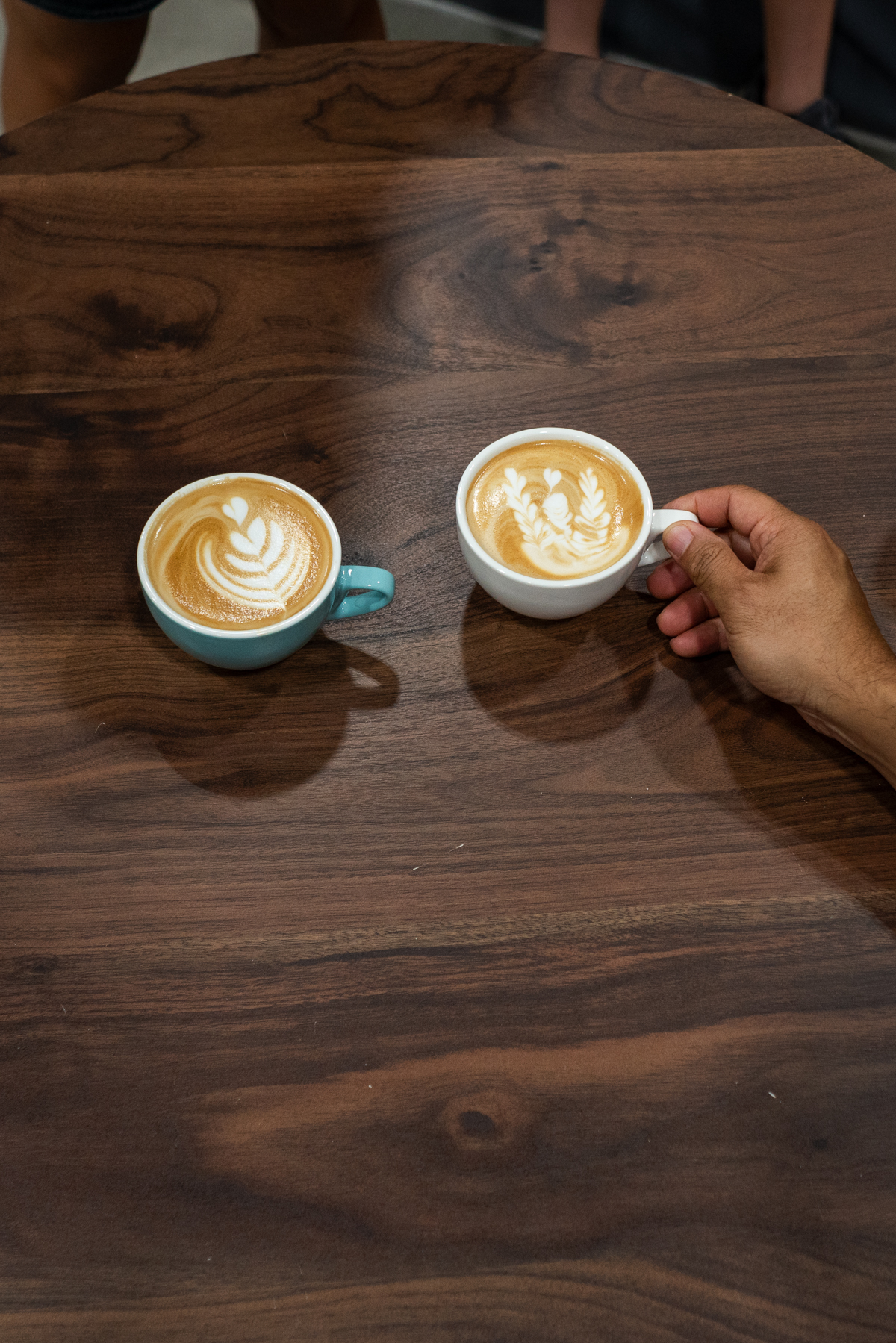 A top-down view of finished latte art cups lined up on dark wood during the Bouldering Baristas throwdown